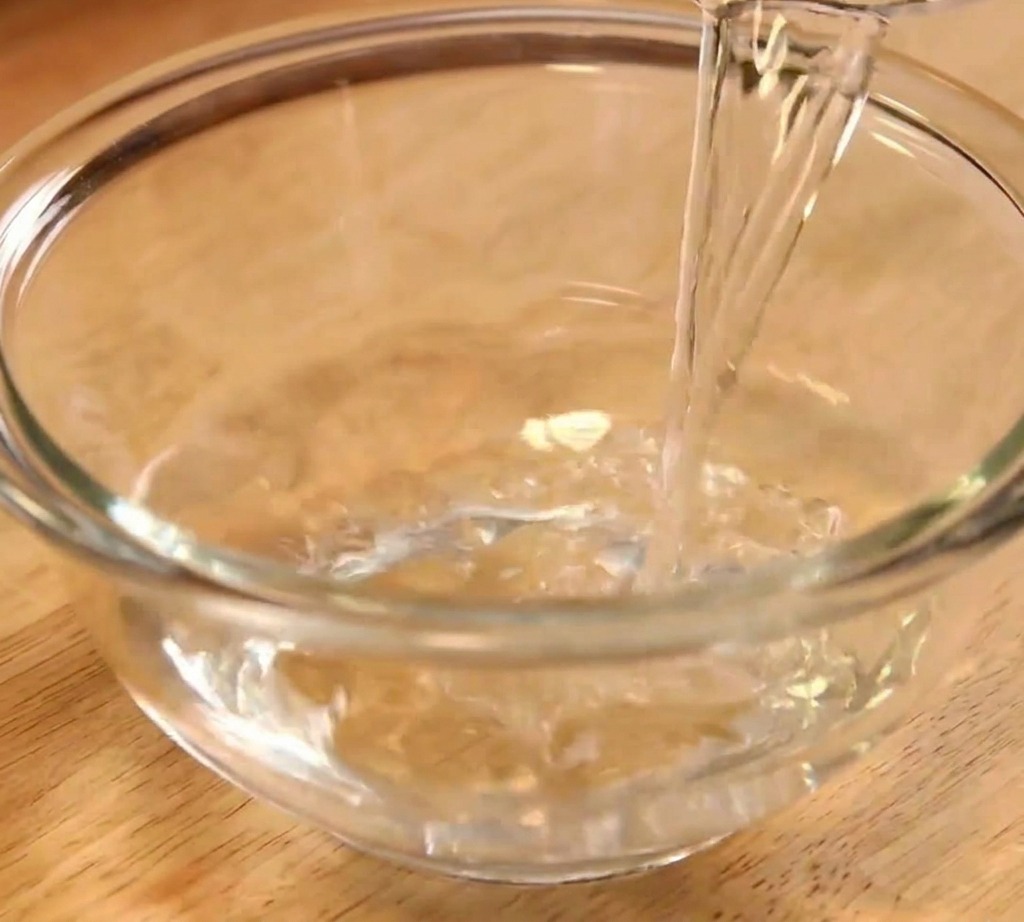 Klares Wasser wird als erster Schritt der Saucenzubereitung in eine transparente Glasschüssel gegossen.