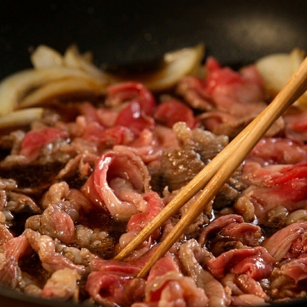 Dünn geschnittenes Rindfleisch und Zwiebeln köcheln in einer blubbernden dunkelbraunen Sauce und werden mit Holzstäbchen umgerührt.