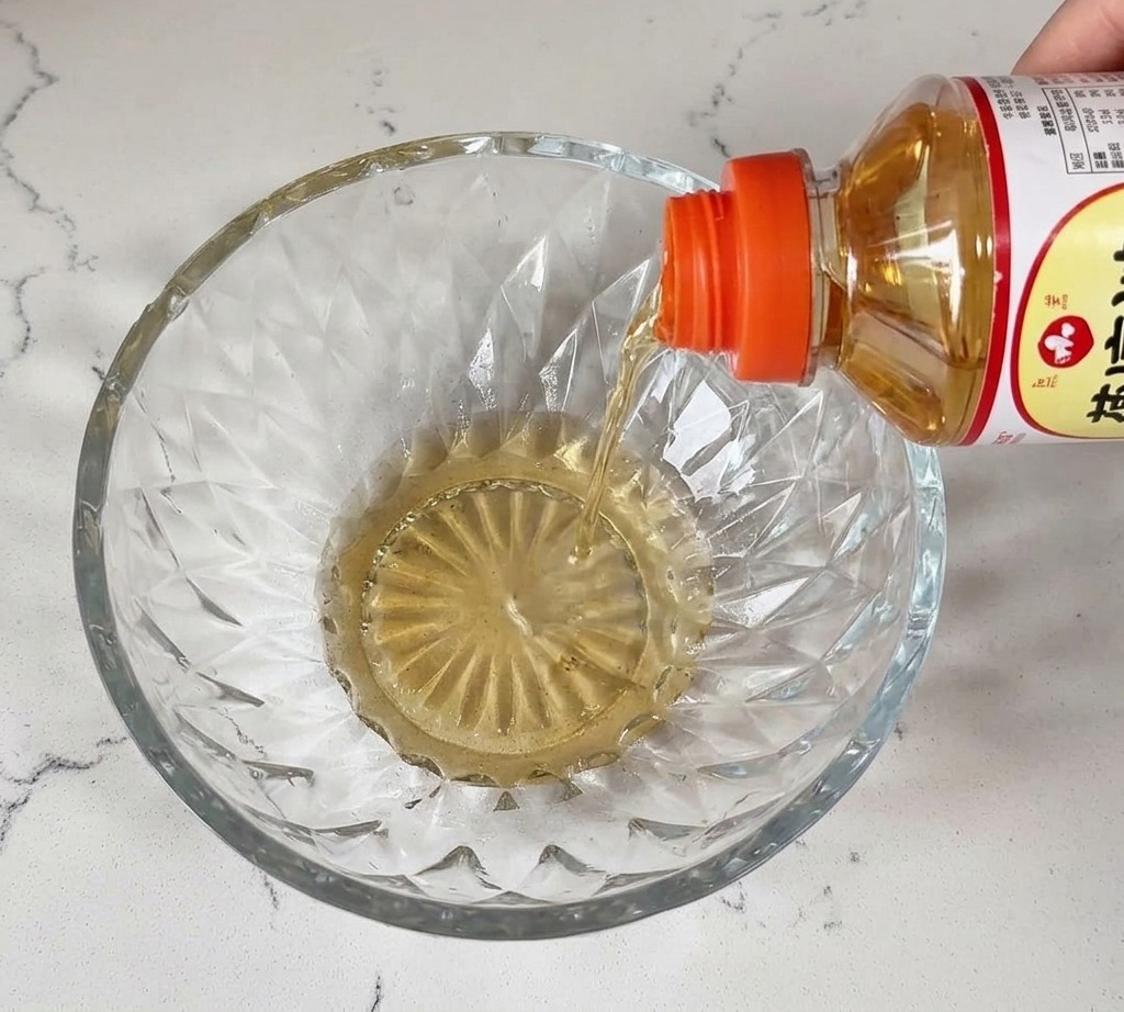 Flüssiges Mirin wird aus einer Flasche in eine Kristallglasschale auf einer weißen Arbeitsplatte gegossen.