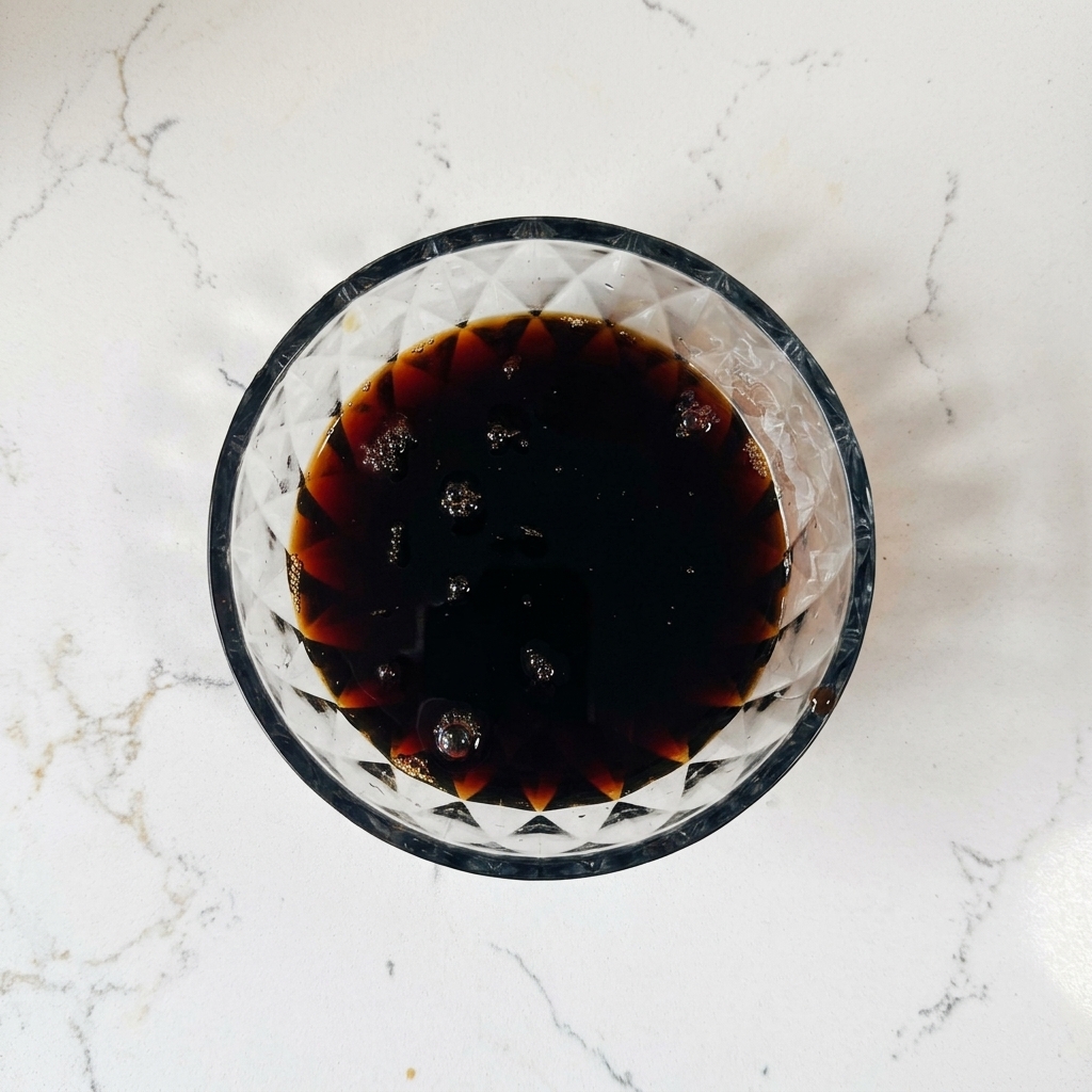 Draufsicht auf eine Glasschale mit einer dunkelbraunen Sauce, die kleine Luftbläschen an der Oberfläche hat.