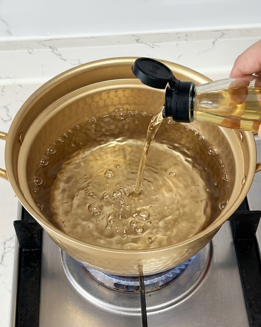 Heller Kochwein wird aus einer Glasflasche in einen goldfarbenen Topf mit kochendem Wasser gegossen.