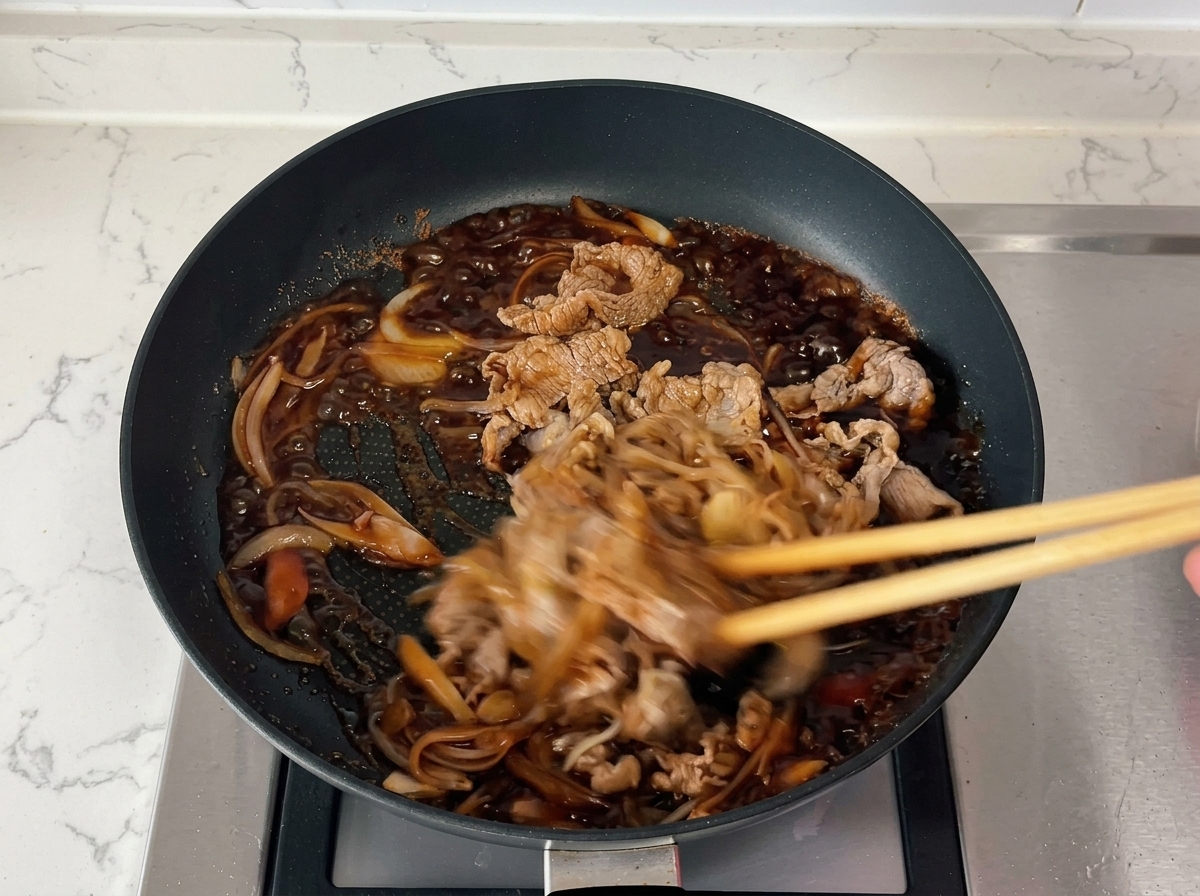 Stäbchen rühren Rindfleisch und Zwiebeln in einer köchelnden, eingedickten dunklen Sauce zügig um.