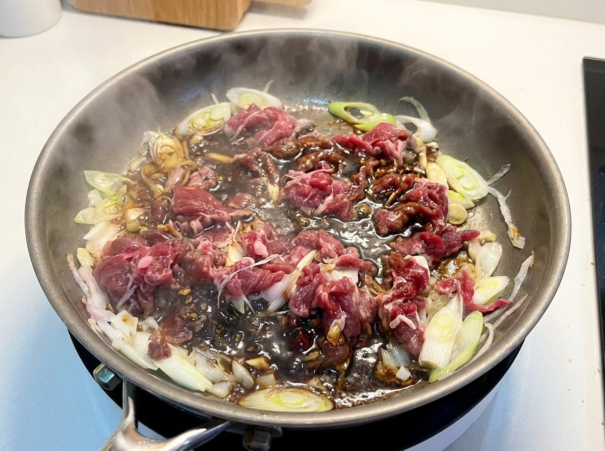 Angebratenes Rindfleisch und Zwiebeln köcheln in einer dunklen, reichhaltigen Sauce in einer Pfanne.