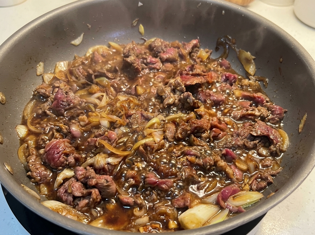 Gebräuntes, dünn geschnittenes Rindfleisch köchelt kräftig mit Zwiebeln in einer blubbernden dunklen Sauce.
