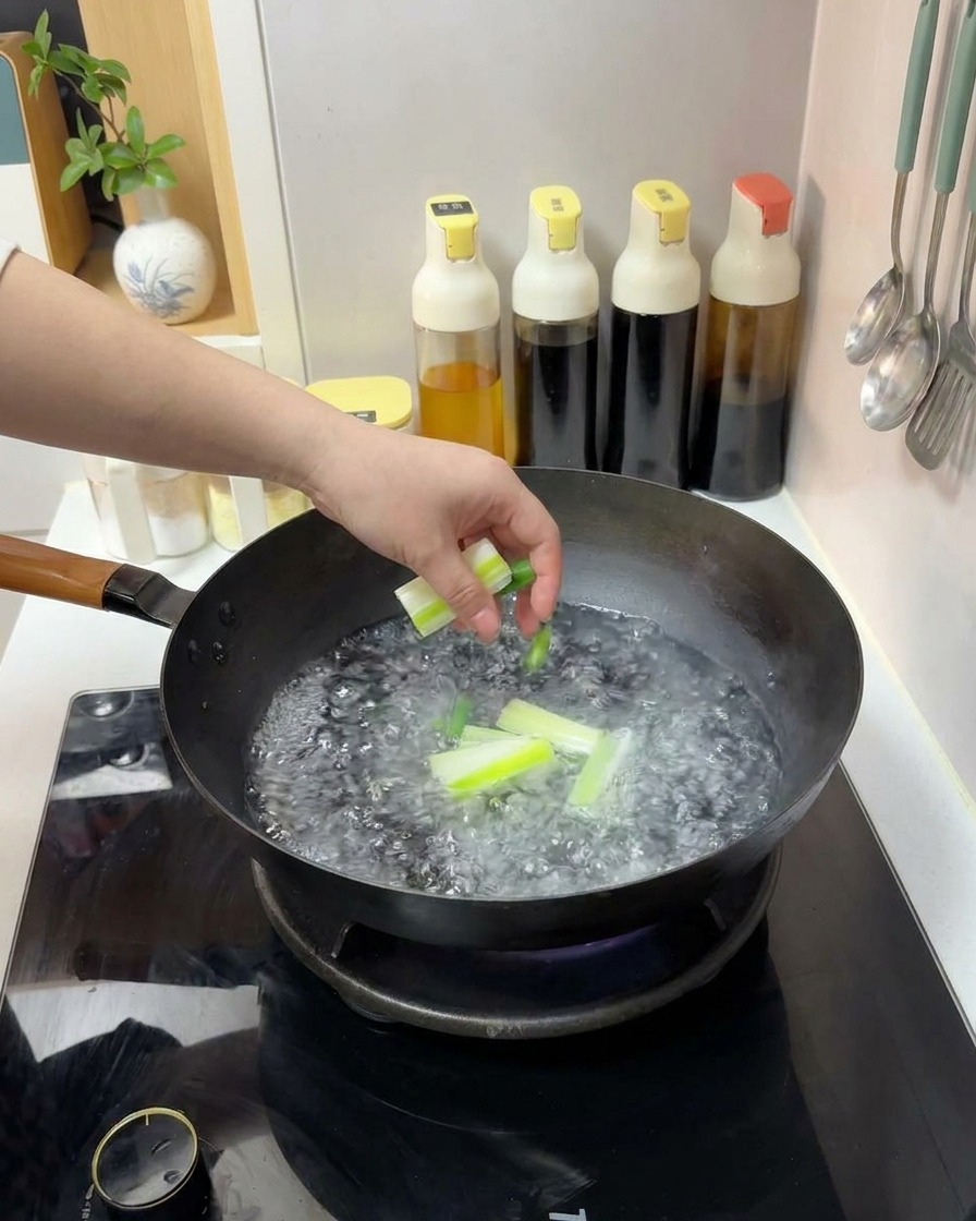 Eine Hand gibt geschnittene Frühlingszwiebeln in einen Wok mit kochendem Wasser.