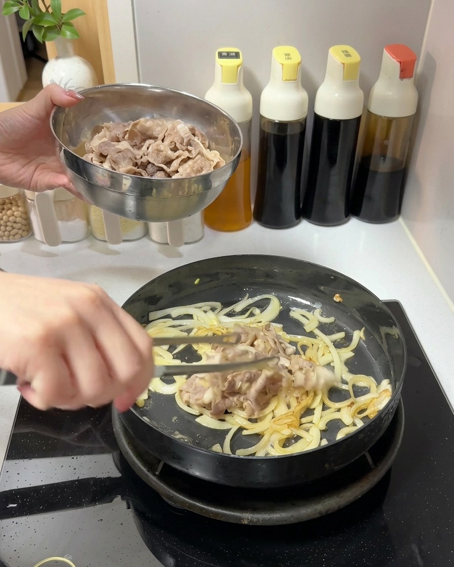 Eine Schüssel mit gekochten Rindfleischscheiben wird in eine Pfanne mit angebratenen Zwiebeln gegeben.