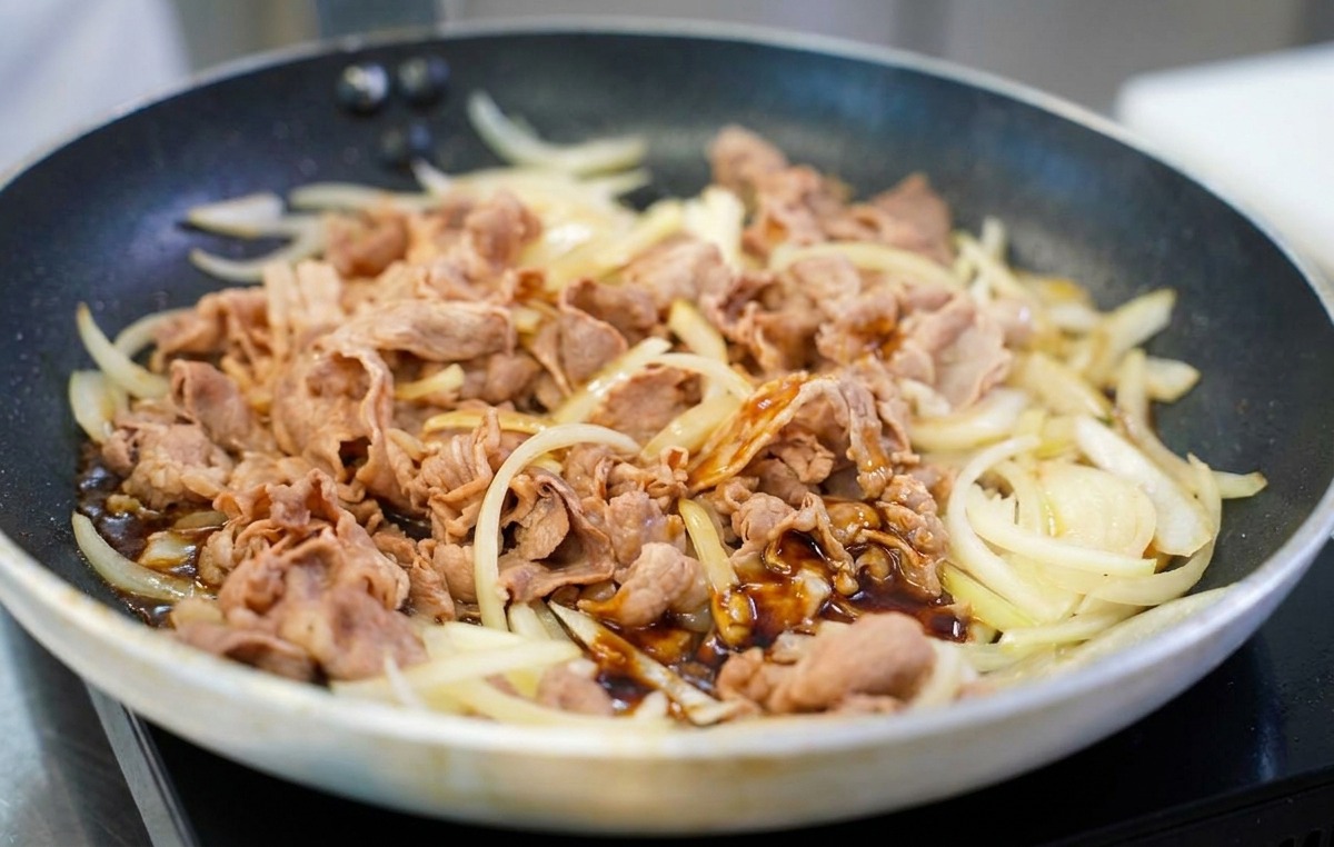 Eine dunkle, glänzende braune Sauce wird über das gebratene Rindfleisch und die Zwiebeln in der Pfanne gegossen.