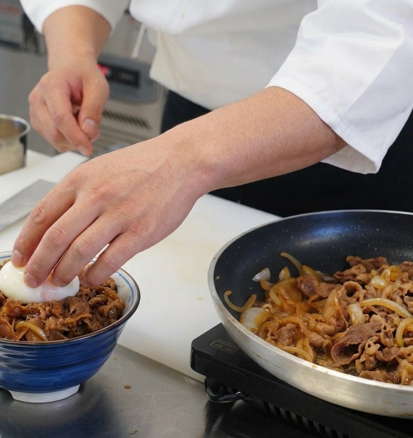Eine Hand setzt ein wachsweich gekochtes Ei mit flüssigem Dotter in die Mitte der fertigen Schüssel mit Rindfleisch und Reis.