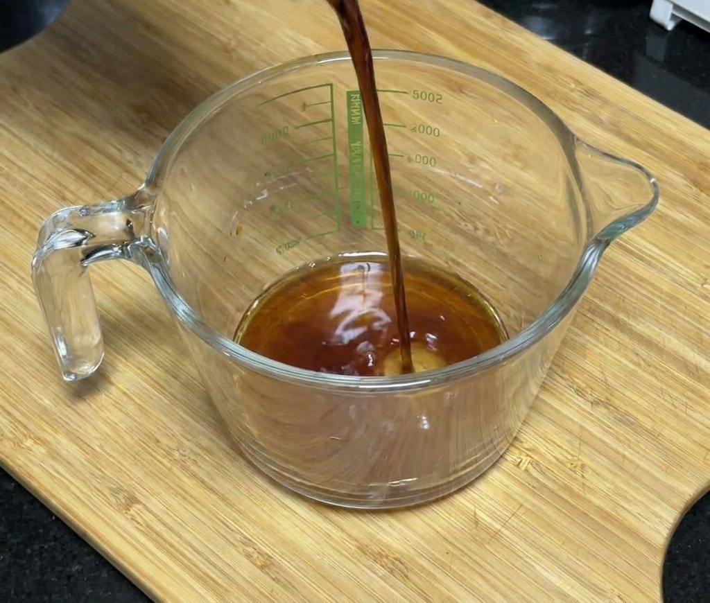 Dunkle Sojasauce wird in einen Messbecher aus Glas gegossen, der Honig und Gewürze enthält.