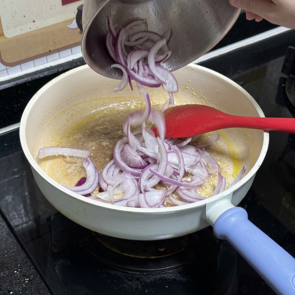 In Streifen geschnittene rote Zwiebeln werden aus einer Edelstahlschüssel in eine weiße Pfanne mit geschmolzener Butter gegeben.