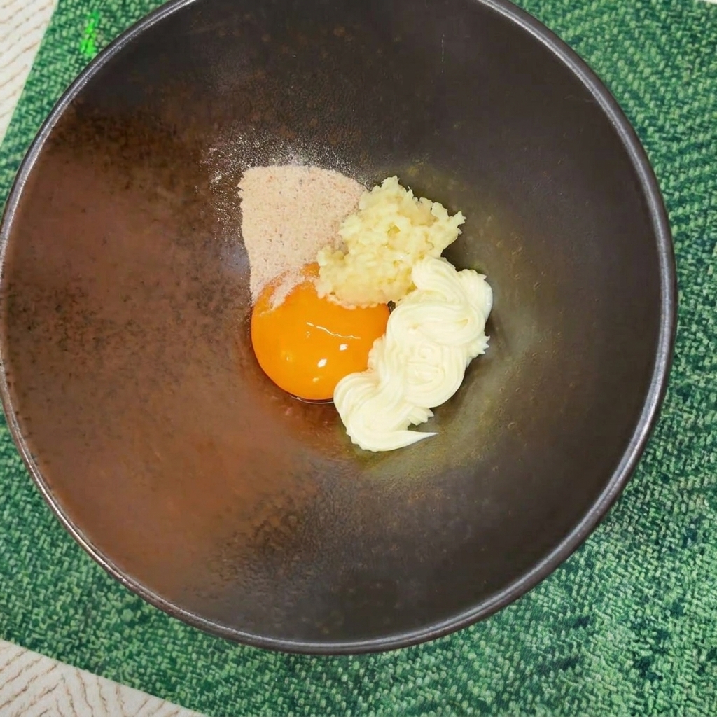 Ramen-Würzpulver über Eigelb und Mayonnaise in einer dunklen Schüssel.
