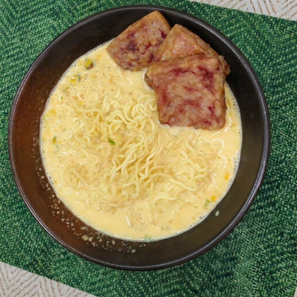 Gekochte Nudeln in gelber Brühe, belegt mit drei Scheiben knusprig gebratenem Frühstücksfleisch.