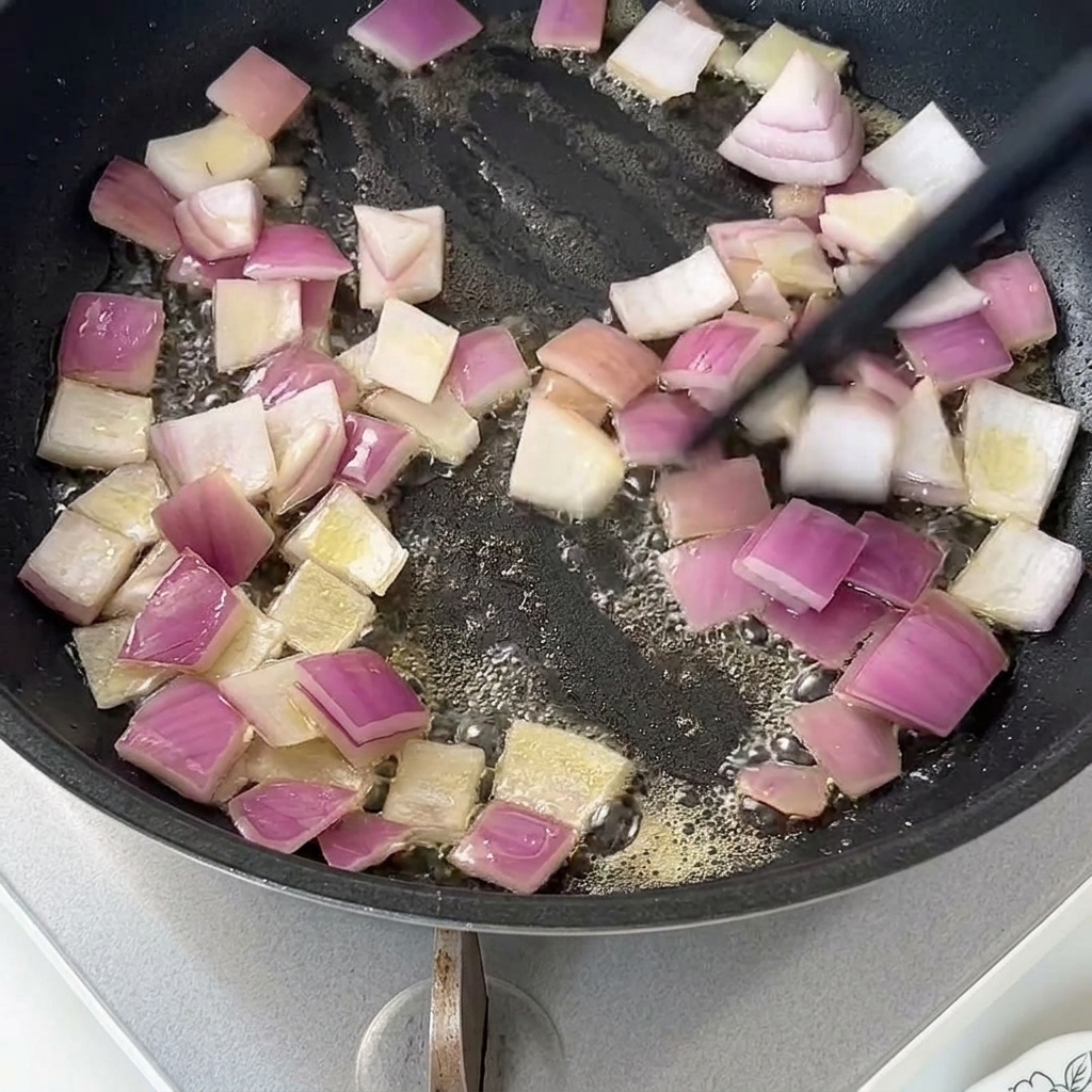 Gewürfelte rote Zwiebeln dünsten in geschmolzener Butter in einer beschichteten Pfanne.
