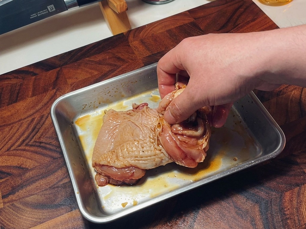Eine Hand vermengt das gewürzte, rohe Hähnchenfleisch in einer Form, um die Gewürze gleichmäßig zu verteilen.