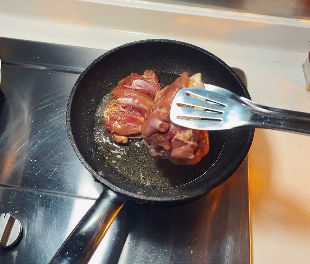Mariniertes Hähnchenfleisch wird mit der Hautseite nach unten in eine heiße Pfanne mit brutzelndem Öl gelegt.