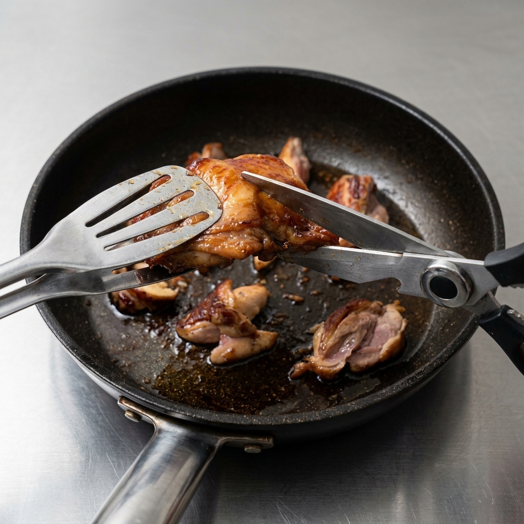 Eine Küchenschere schneidet das angebratene Hähnchenfleisch direkt in der Pfanne in kleine, gleichmäßige Stücke.