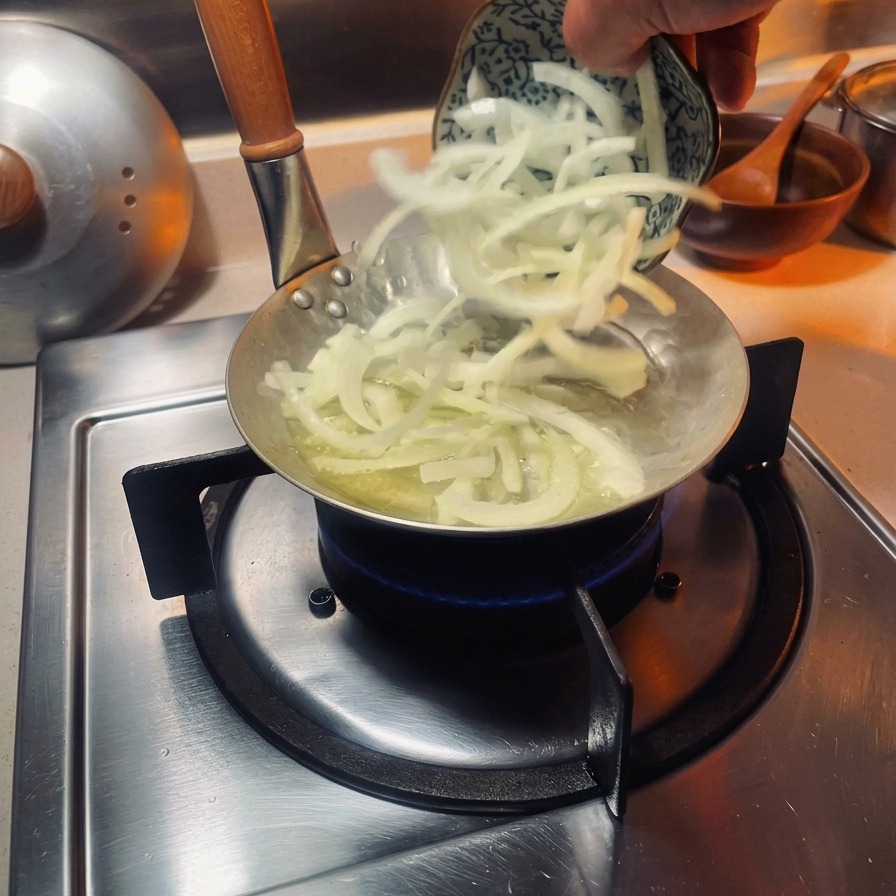 Feine Zwiebelstreifen werden in eine kleine, spezielle Oyakodon-Pfanne auf einem Gasherd gegeben.