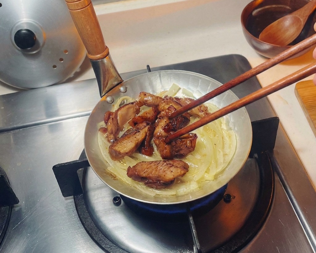 Angebratene Hähnchenstücke werden mit Stäbchen gleichmäßig auf dem Zwiebelbett in einer kleinen Pfanne verteilt.
