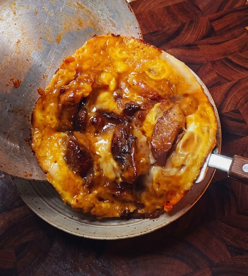 Das fertige Hähnchen-Ei-Topping wird vorsichtig aus der Metallpfanne auf eine Schüssel mit fluffigem weißen Reis gleiten gelassen.