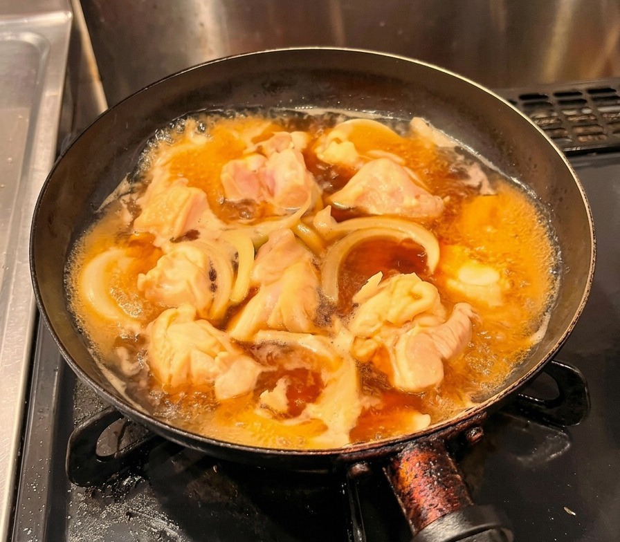 Verquirlte gelbe Eier werden in einem gleichmäßigen Strom über das köchelnde Hähnchen und die Zwiebeln in einer schwarzen Pfanne gegossen.