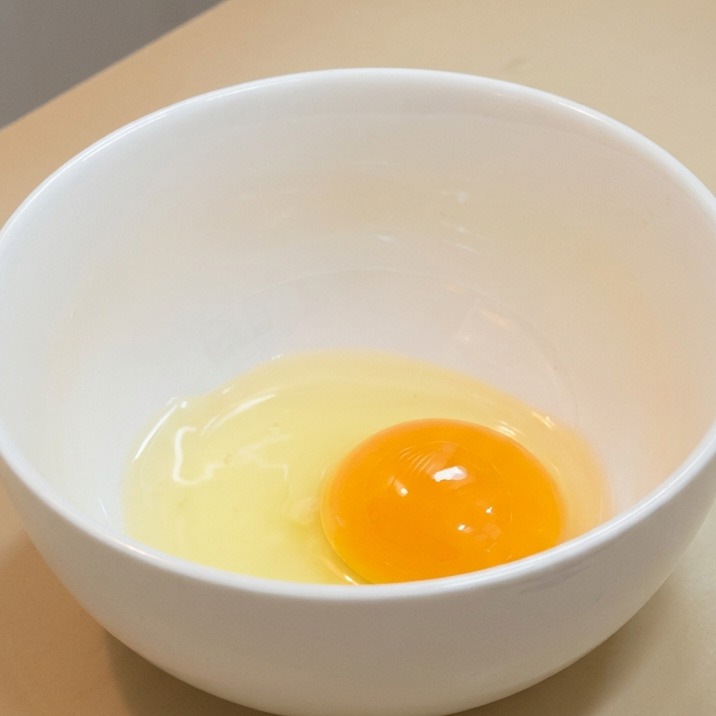 Ein rohes Eigelb und klares Eiweiß liegen in einer weißen Keramikschale.