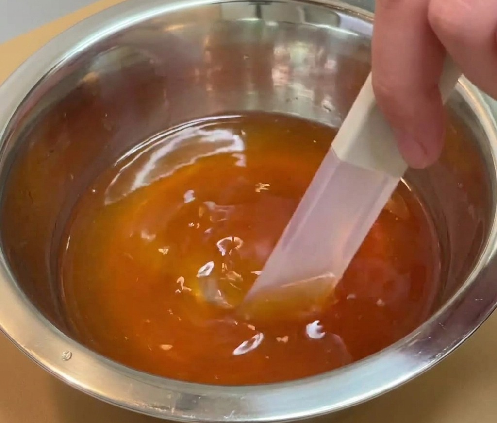 Eine Hand verrührt eine dunkle, durchscheinende Würzsauce mit einem Spatel in einer Edelstahlschüssel.