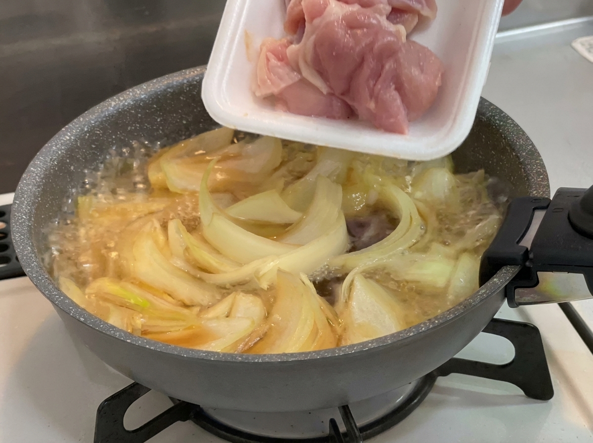 Rohe, rosa Stücke von der Hähnchenkeule werden aus einer Verpackung in die Pfanne zu den köchelnden Zwiebeln gegeben.