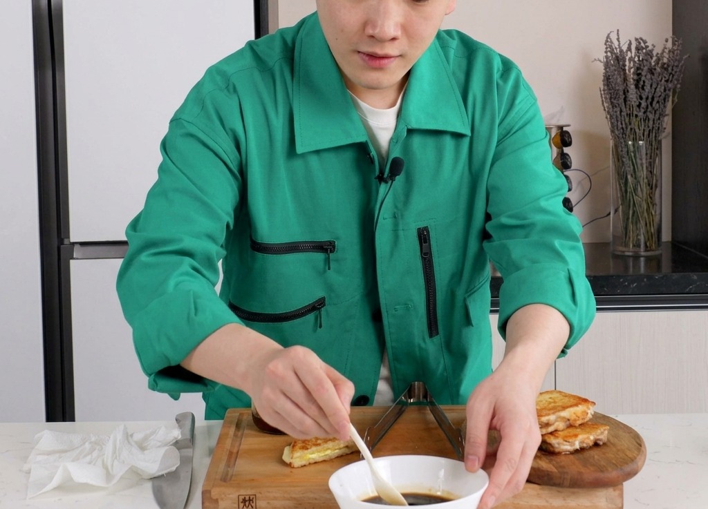 Eine Person verrührt eine dunkle Sauce auf Sojabasis mit einem kleinen weißen Löffel in einer Keramikschale.
