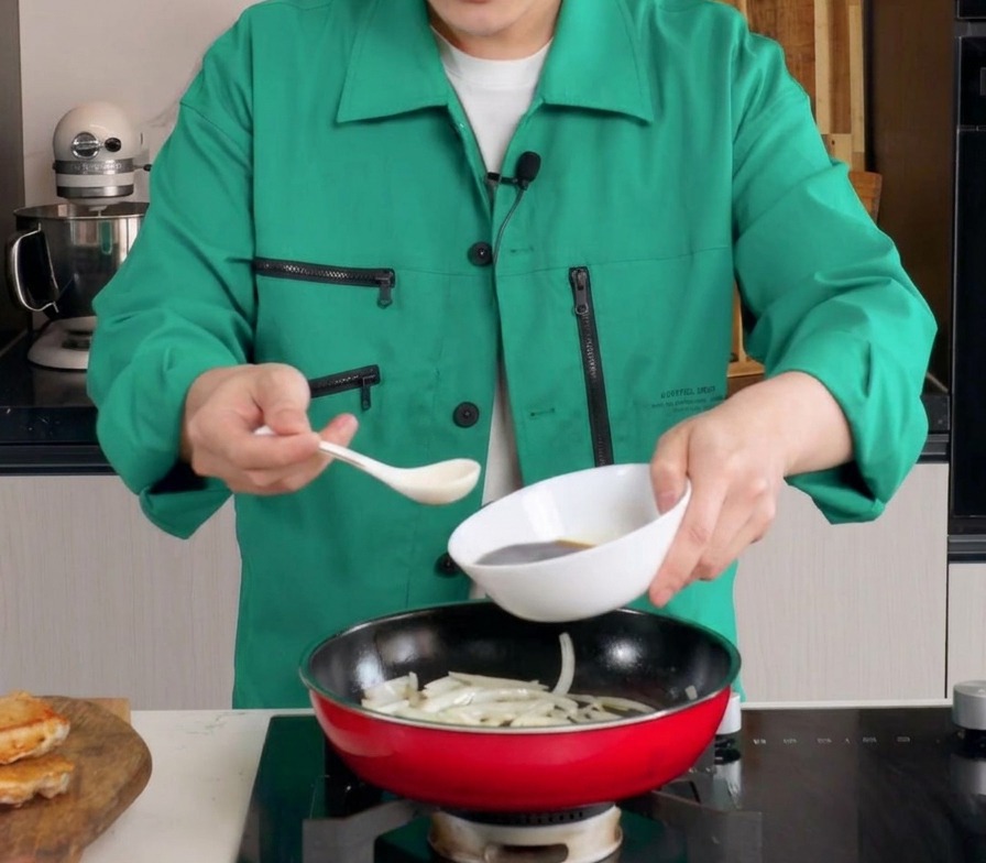 Die dunkle Sauce wird aus einer weißen Schale in eine Pfanne zu den weichen Zwiebelstreifen gegossen.