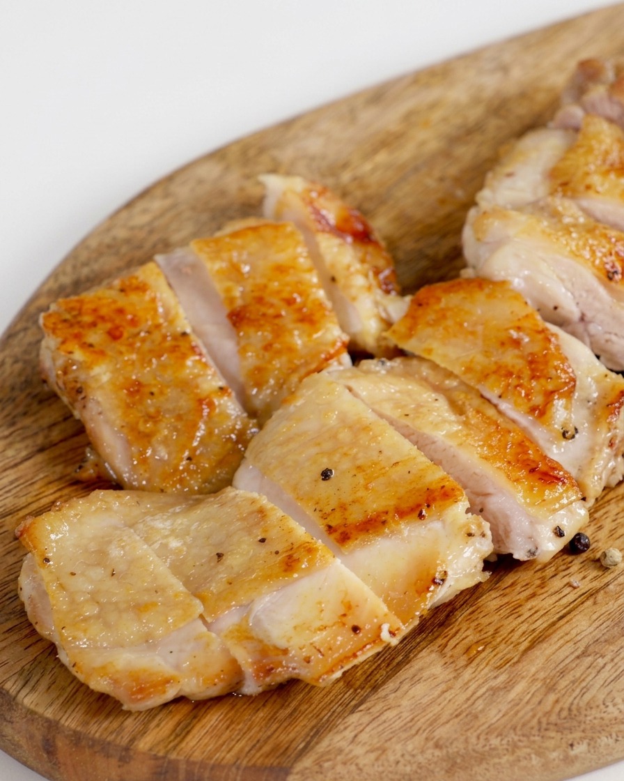 Das knusprig gebratene Hähnchenfleisch wird auf einem Holzbrett mit einem scharfen Messer in gleichmäßige Streifen geschnitten.
