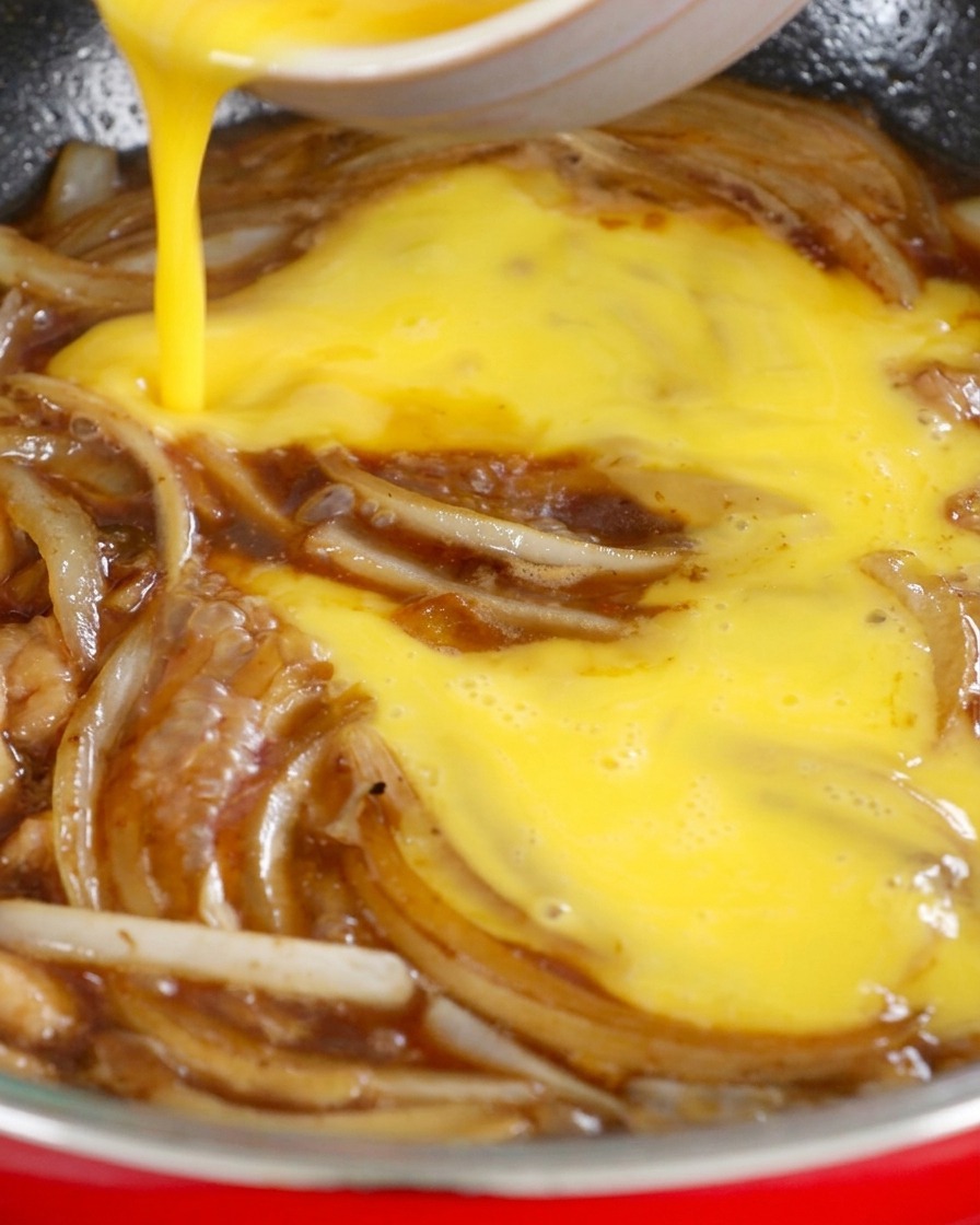 Die leicht verquirlten Eier werden kreisförmig in die Pfanne zu den Zwiebeln und der kochenden Sauce gegossen.