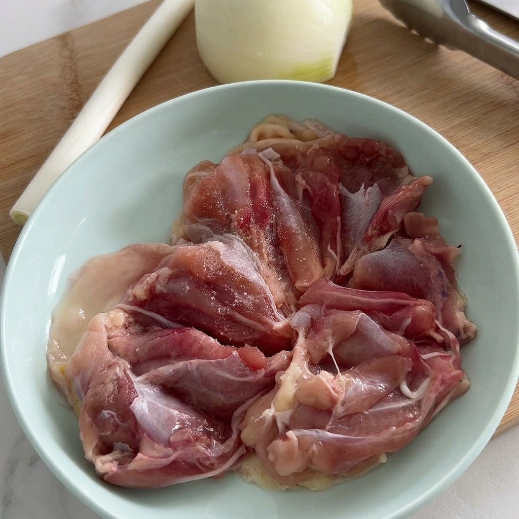 Rohe Hähnchenkeulenfilets in einer blassblauen Schüssel, die mit Salz und frisch gemahlenem schwarzen Pfeffer gewürzt werden.