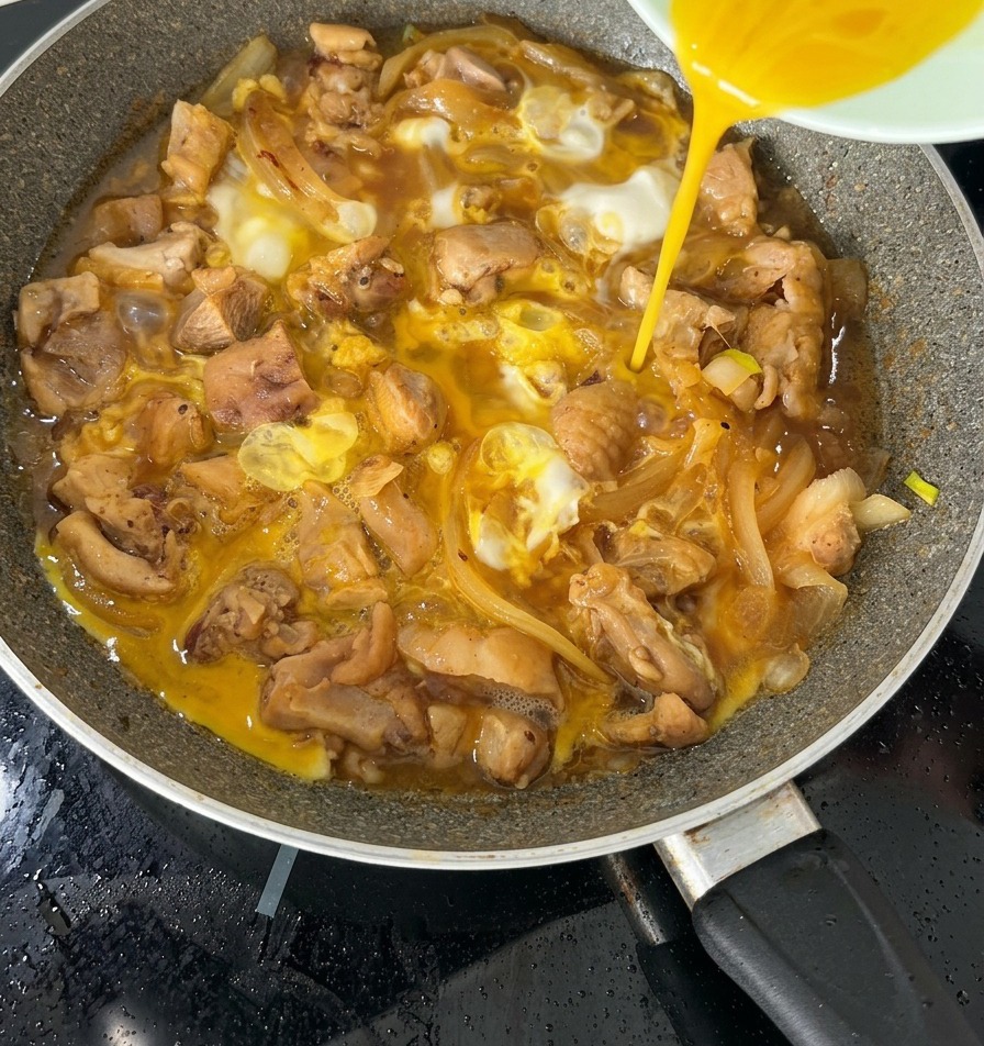 Die zweite Hälfte einer verquirlten Eimischung wird über ein fast fertiges Oyakodon in einer Pfanne gegossen.