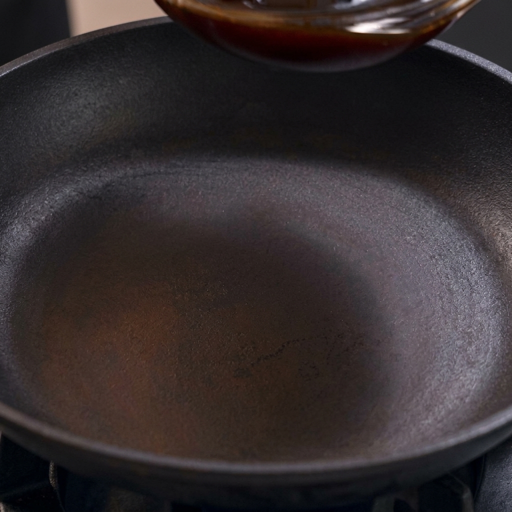 Eine dunkle, süß-salzige Oyakodon-Sauce wird in eine eingebrannte schwarze Pfanne auf dem Herd gegossen.