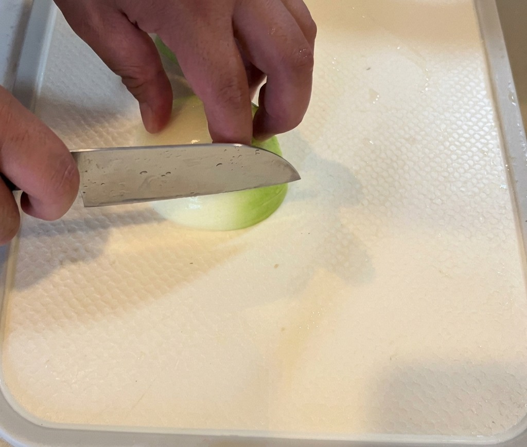 Eine Person schneidet eine weiße Zwiebel in feine Streifen auf einem weißen Schneidebrett.
