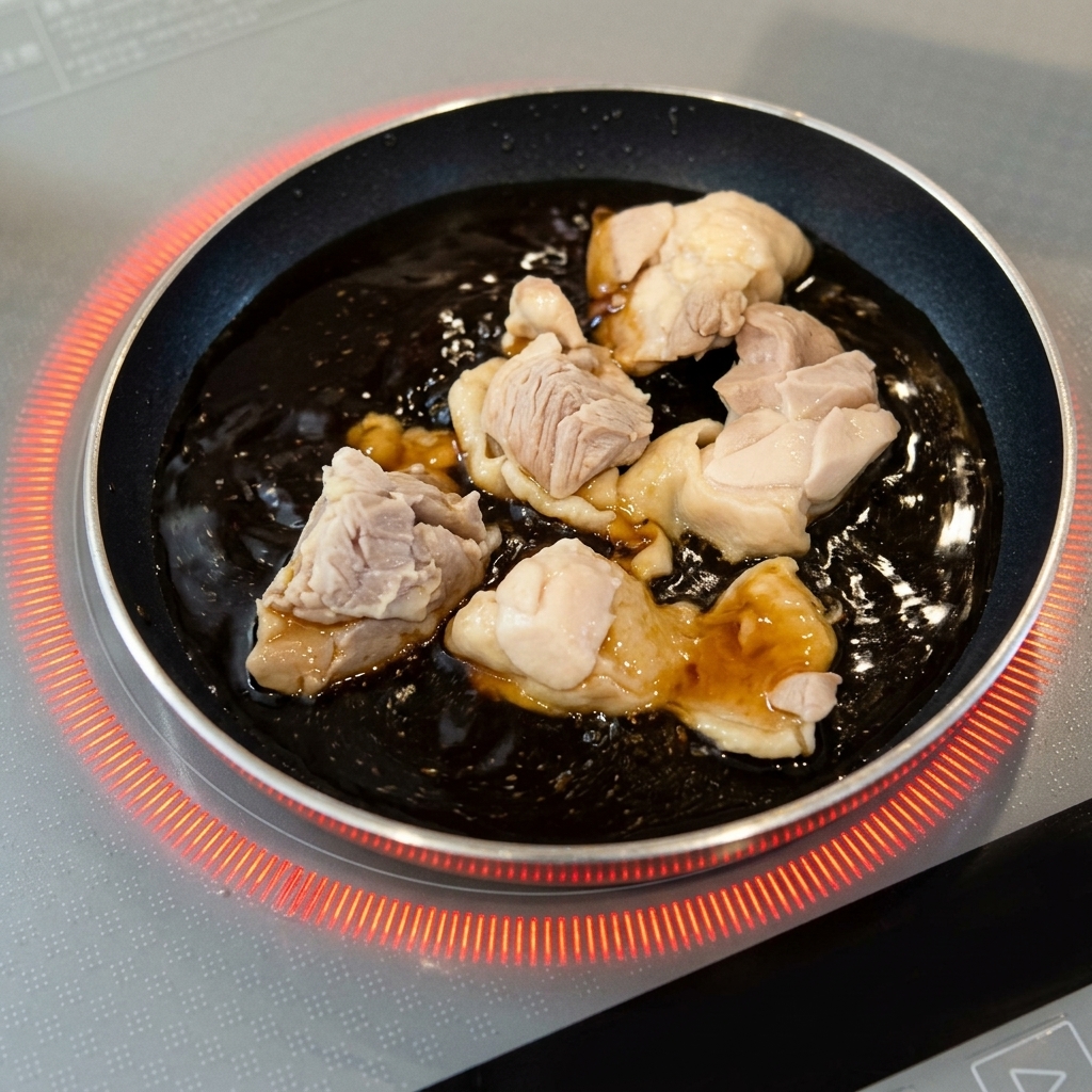 Blanchierte Hähnchenstücke köcheln in einer brodelnden, dunkelbraunen Sauce in einer kleinen runden Pfanne.