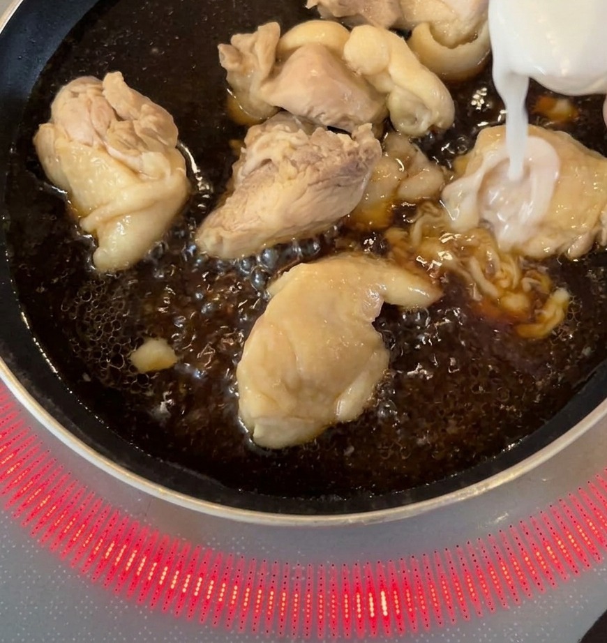 Weiße Zwiebelstreifen werden zu den in dunkler Sauce köchelnden Hähnchenstücken in die Pfanne gegeben.
