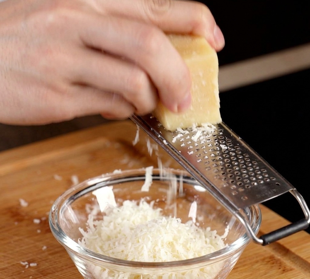 Ein Block Parmesan wird direkt in eine kleine Schüssel mit einem rohen Eigelb gerieben.