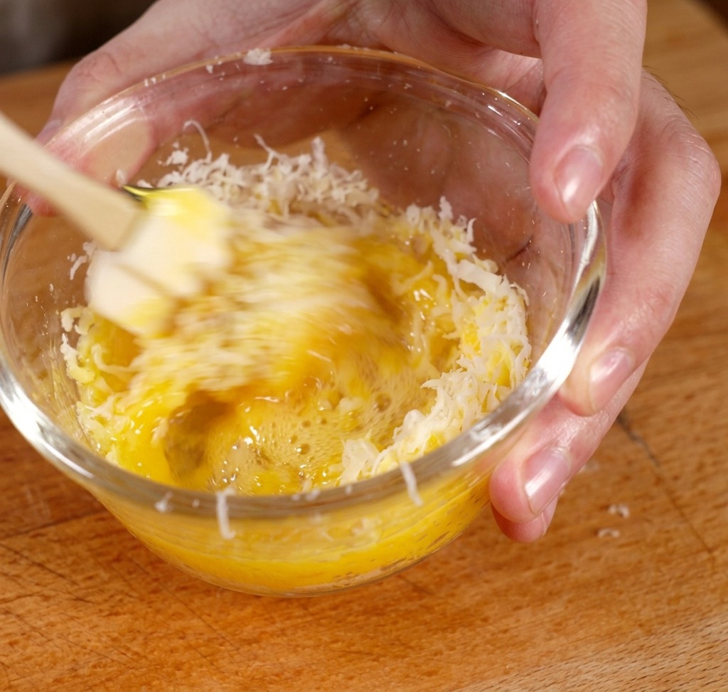 Eigelb und geriebener Käse werden in einer Glasschüssel zu einer dicken, gelben Paste verrührt.