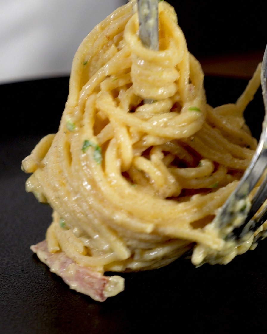 Cremige Spaghetti und Speckstücke werden fest um eine Fleischgabel gedreht, um ein Nest zum Servieren zu bilden.