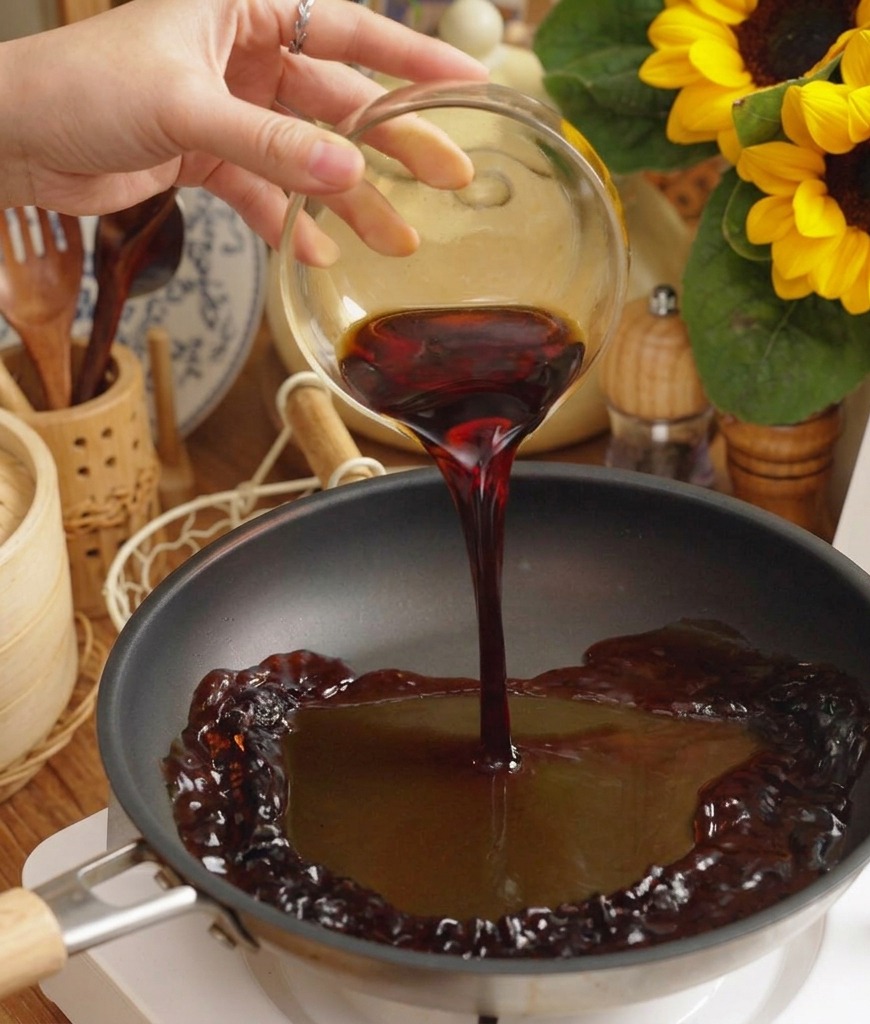 Dunkle, würzige Sauce wird aus einer Glasschüssel in eine schwarze Pfanne auf einer weißen elektrischen Herdplatte gegossen.