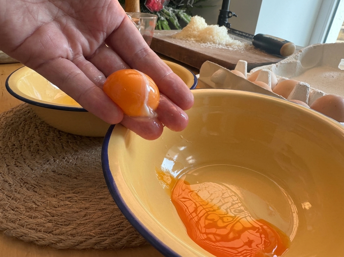 Eine Hand trennt ein leuchtend orangefarbenes Eigelb über einer gelben Schüssel.