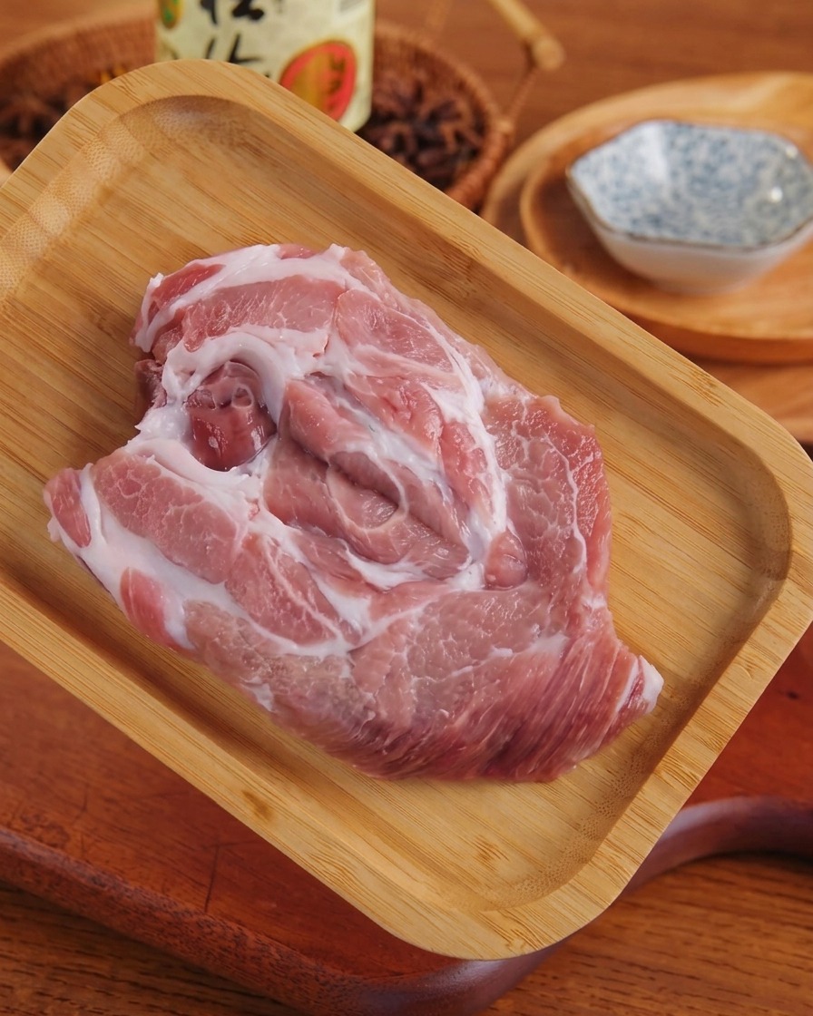 Ein flach geklopftes Stück rohes, marmoriertes Schweinefleisch liegt nach dem Bearbeiten auf einem Holztablett.