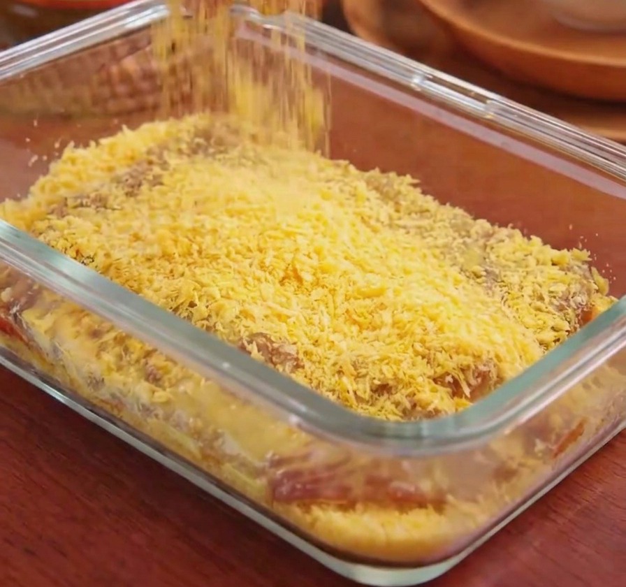 Eine Hand streut goldgelbe Panko-Brotkrumen über ein Schweineschnitzel in einer Glasschale.