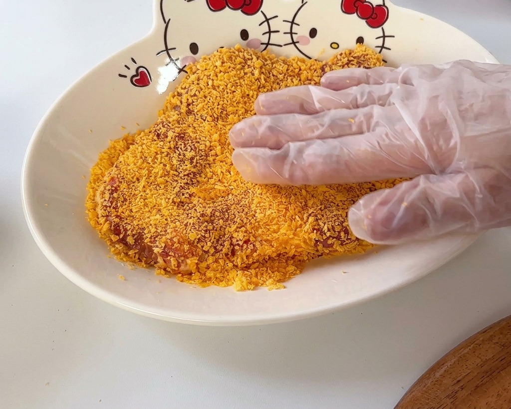 Eine Hand drückt ein Schweineschnitzel in einer Schüssel in eine Schicht goldgelbes Panko-Paniermehl.