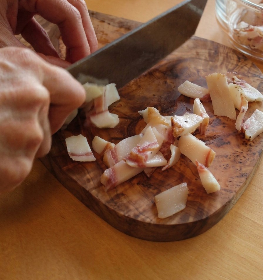 Guanciale wird in gleichmäßige Streifen geschnitten, die Fett- und Fleischschichten zeigen.