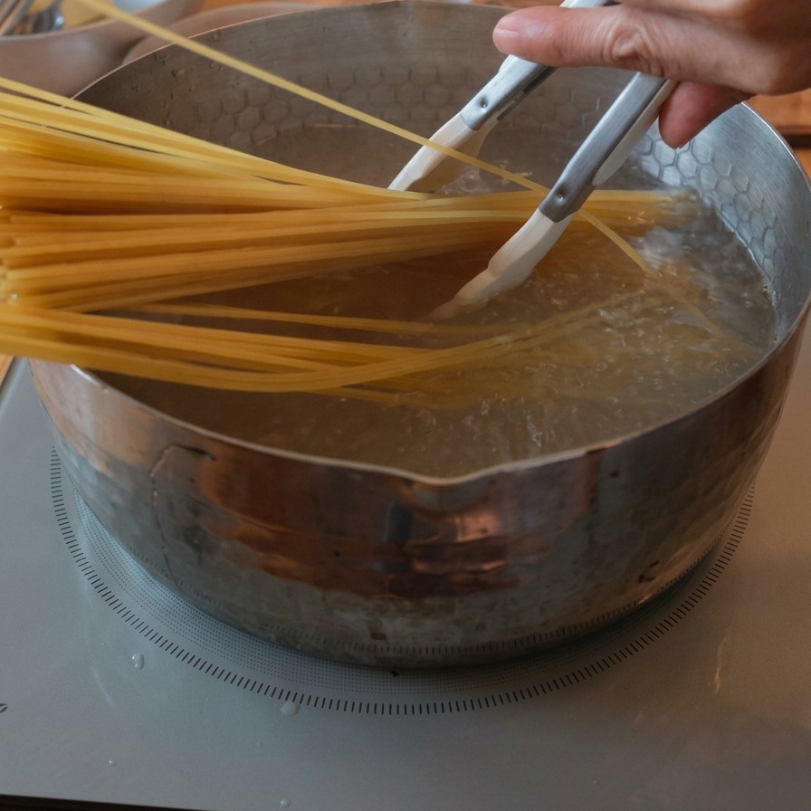 Spaghetti werden mit einer Zange in kochendes Wasser getaucht.