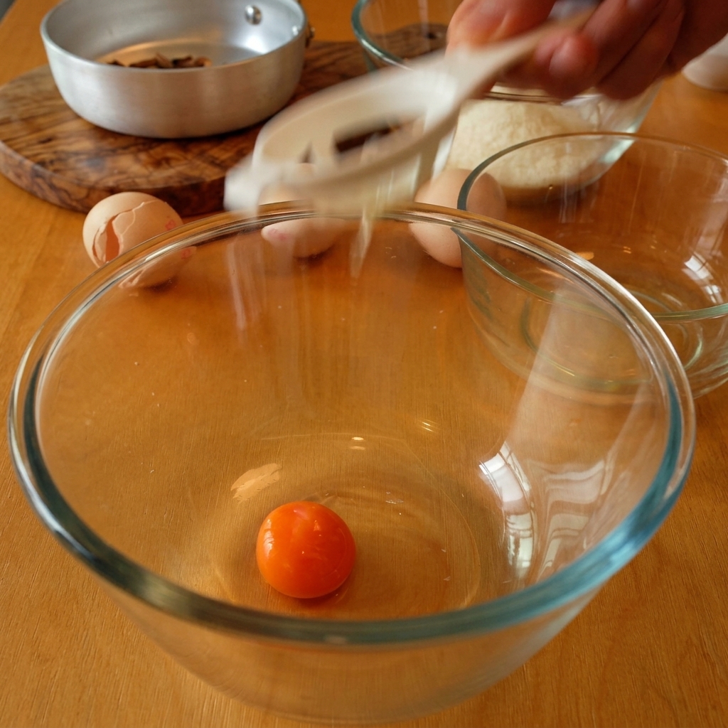 Ein oranges Eigelb in einer Glasschale, während das Eiweiß abtropft.