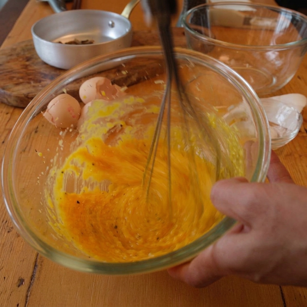 Heißes Pastawasser wird unter Rühren zur Ei-Käse-Mischung gegeben.