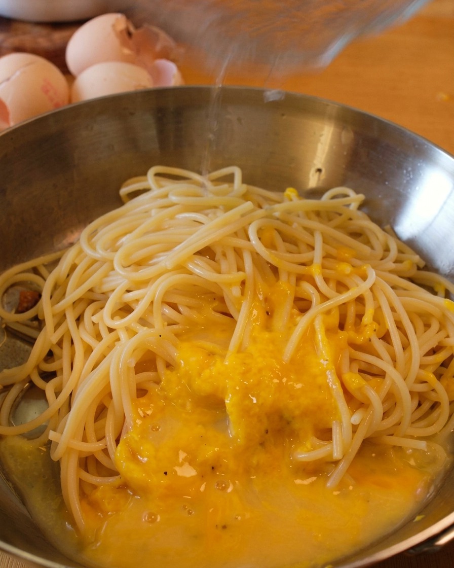 Spaghetti in der Pfanne werden mit Sauce und einem Schuss Nudelwasser vermengt.